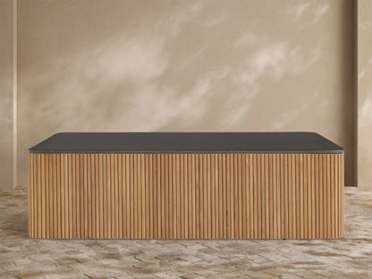 Pompeii Outdoor Coffee Table with a dark gray concrete top and slatted natural teak wood base, set against a beige wall.