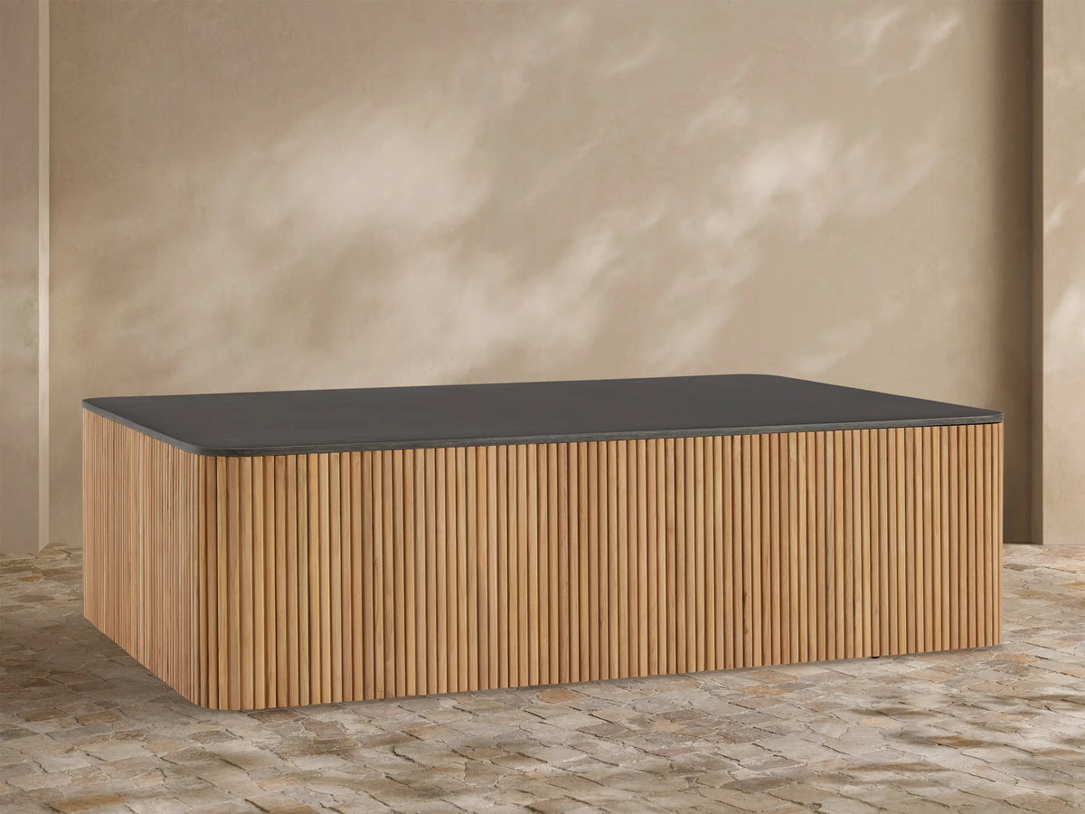 Pompeii Outdoor Coffee Table with a dark gray concrete top and slatted natural teak wood base, set against a beige wall.
