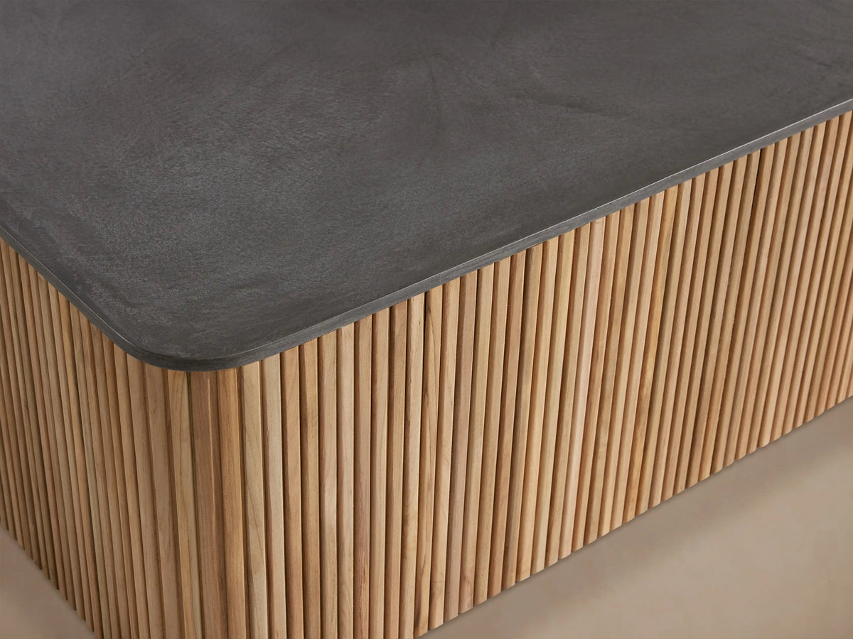 Rectangular Pompeii Outdoor Coffee Table with dark grey concrete top & natural teak wood slatted base on a stone patio.