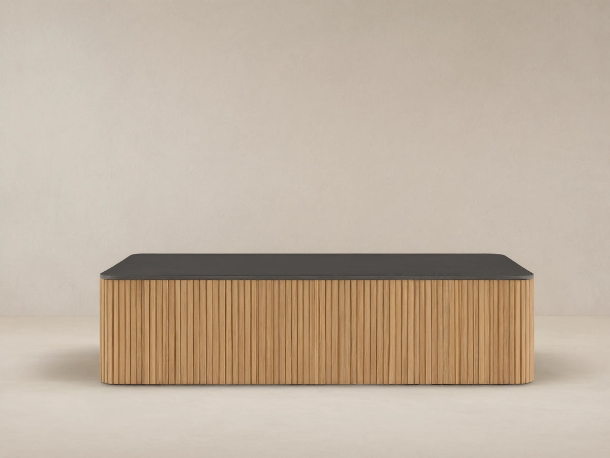 Pompeii Outdoor Coffee Table with a dark gray concrete top and slatted natural teak wood base, set against a beige wall.