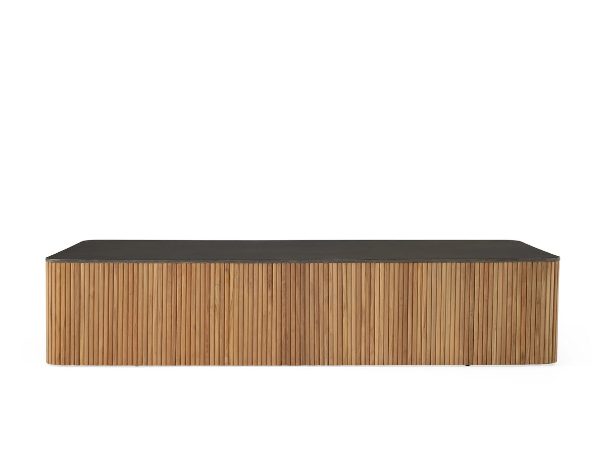 Pompeii Outdoor Coffee Table with a smooth black concrete top and vertical slatted reclaimed teak base, set against a coastal backdrop.