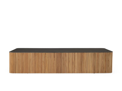 Pompeii Outdoor Coffee Table with a smooth black concrete top and vertical slatted reclaimed teak base, set against a coastal backdrop.