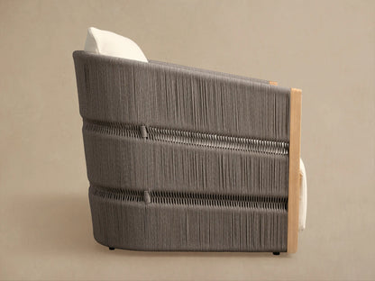 Side view of Manadala Outdoor Swivel Chair. Dark gray handwoven rope texture, light teak wood frame, and ivory cushion.