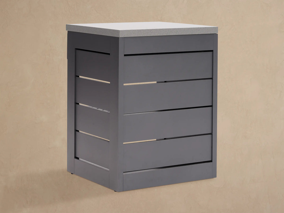 Dark gray outdoor aluminum modular kitchen cabinet with light gray sintered stone top, single drawer, and two slatted shelves.