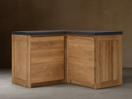 Modular kitchen corner cabinet made of natural teak wood with a dark gray sintered stone countertop, on a tiled floor.