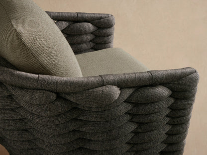 Melbourne Outdoor Swivel Chair, dark charcoal woven frame, light beige textured cushions, black swivel base, on stone floor.