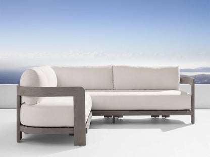 Milos outdoor sofa with light cream water-repellent cushions on a gray wood frame, overlooking a serene ocean view.