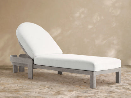 Milos Outdoor Chaise with weathered gray teak frame and thick white cushions, adjustable rounded back, on a stone patio.