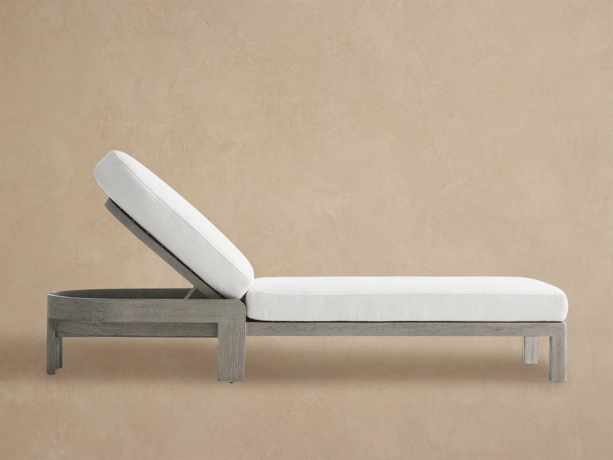 Milos Outdoor Chaise with weathered gray teak frame and thick white cushions, adjustable rounded back, on a stone patio.