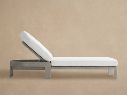 Milos Outdoor Chaise with weathered gray teak frame and thick white cushions, adjustable rounded back, on a stone patio.