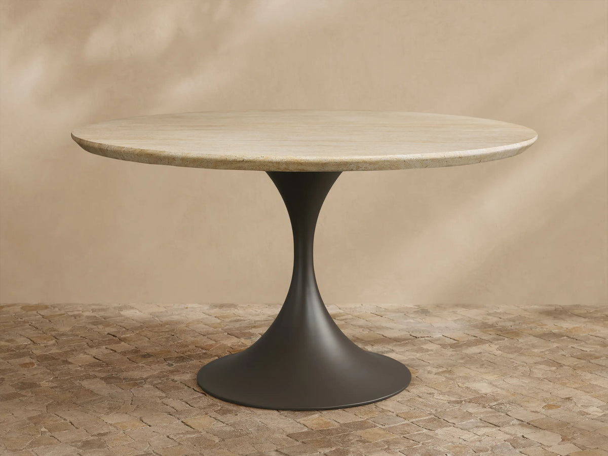 Outdoor round dining table with light beige textured stone top & dark gray flared pedestal Launette base on a tiled patio.