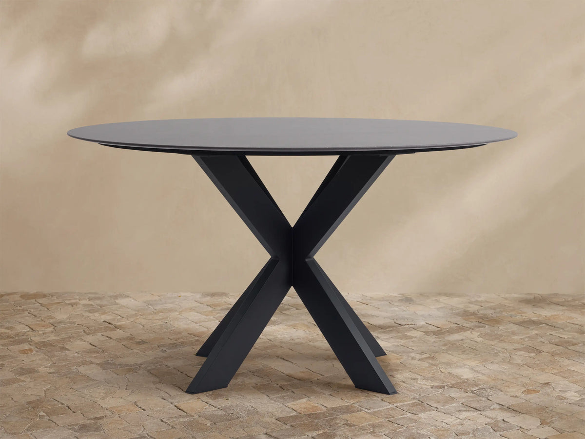 Round dark grey outdoor dining table with a black X-shaped Apex base on a light brown tiled patio.