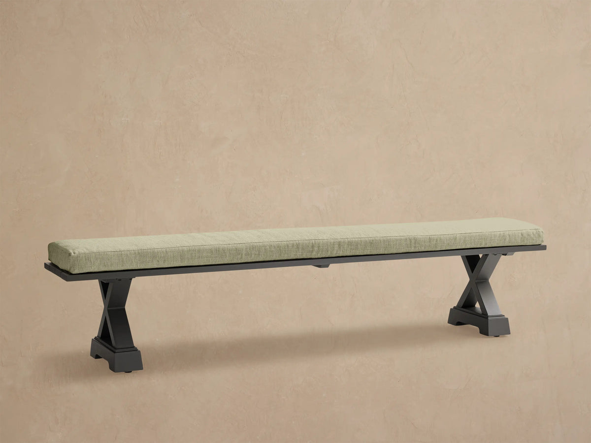 Montego Outdoor Aluminum Dining Bench with dark frame and Eden Sage cushion, against a wooden wall on a patio.