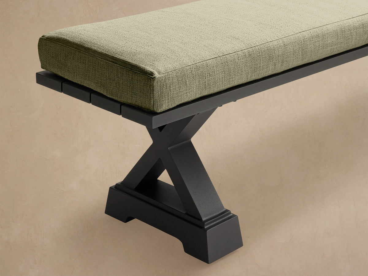 Montego Outdoor Aluminum Dining Bench, dark X-frame, long rectangular Eden Sage light green cushion, angled view on a beige background.