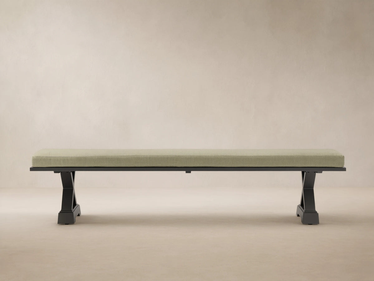 Montego Outdoor Aluminum Dining Bench with dark frame and Eden Sage cushion, against a wooden wall on a patio.