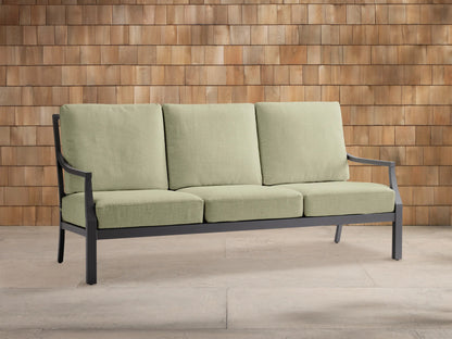 Montego outdoor aluminum sofa with dark gray frame and three light green Eden Sage cushions, on a light patio against a wood wall.