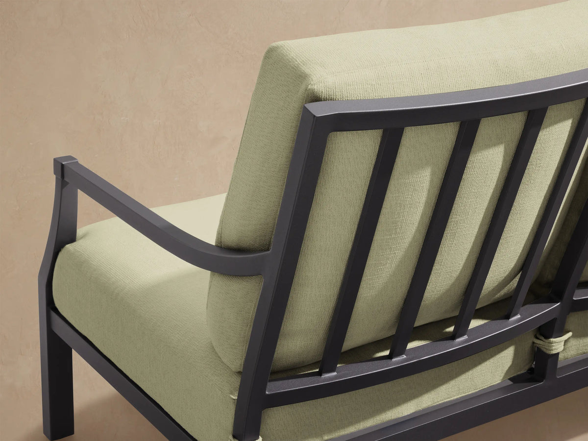 Montego Outdoor Aluminum Sofa with dark gray frame and three light green Eden Sage cushions, on a patio with a shingle wall.