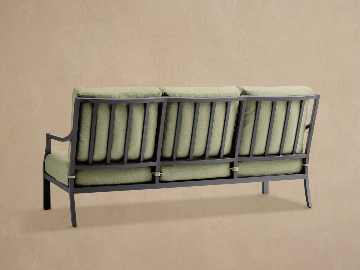 Angled close-up of Montego Outdoor Aluminum Sofa in Eden Sage. Dark gray frame with slatted back, light green cushions.
