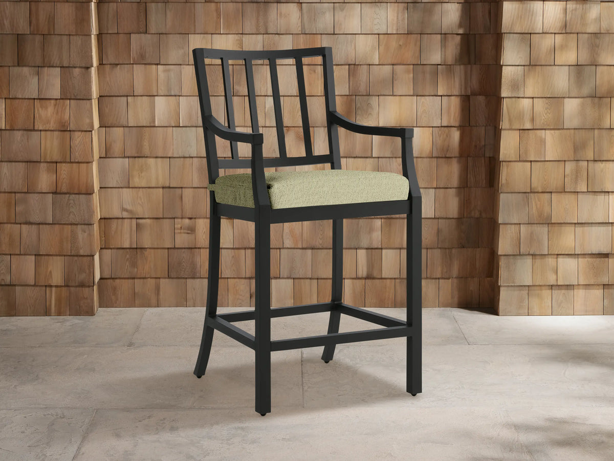 Montego Outdoor Aluminum Counter Stool, dark gray, with slatted back, armrests & light green Eden Sage cushion on a patio.