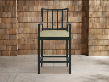 Montego Outdoor Aluminum Counter Stool, dark gray, with slatted back, armrests & light green Eden Sage cushion on a patio.