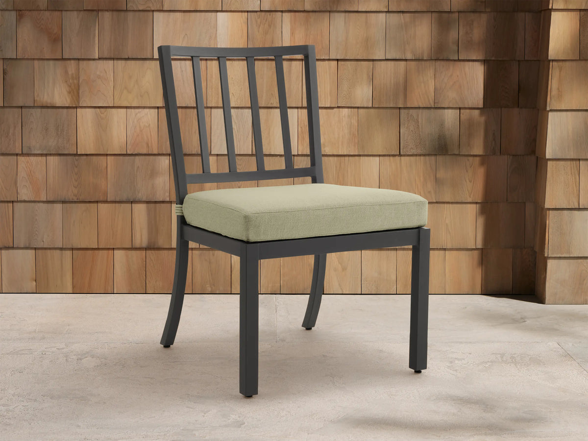 Montego Outdoor Aluminum Dining Side Chair with dark gray frame & light sage cushion, angled against a wood shingle wall.