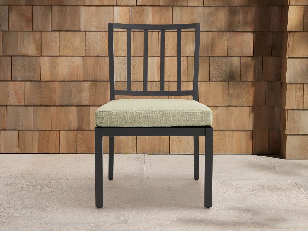 Montego Outdoor Aluminum Dining Side Chair with dark gray frame & light sage cushion, angled against a wood shingle wall.