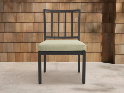 Montego Outdoor Aluminum Dining Side Chair with dark gray frame & light sage cushion, angled against a wood shingle wall.