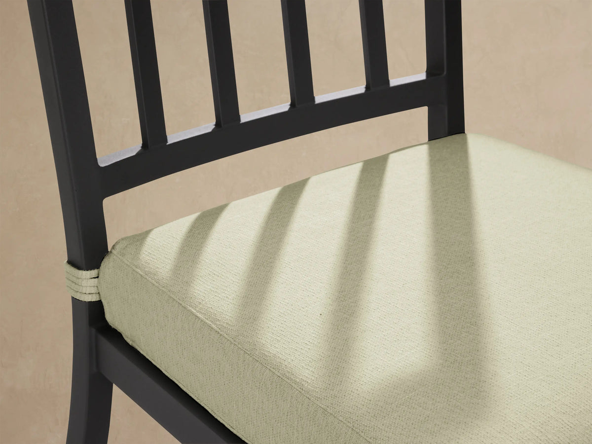 Front view of Montego Outdoor Aluminum Dining Side Chair with matte black frame, vertical slats, and light green Eden Sage cushion on patio.