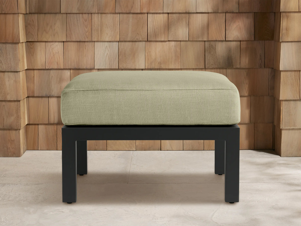 Montego Outdoor Aluminum Ottoman with light sage green rectangular cushion on a dark gray aluminum frame, front view on patio.