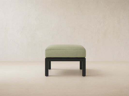 Montego Outdoor Aluminum Ottoman with light sage green rectangular cushion on a dark gray aluminum frame, front view on patio.