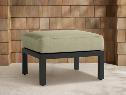 Montego Outdoor Aluminum Ottoman with light sage green rectangular cushion on a dark gray aluminum frame, front view on patio.
