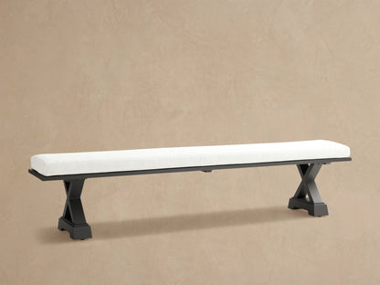 Montego Outdoor Aluminum Dining Bench, front view. White cushion on black aluminum frame with angled trestle legs. Wooden wall background.