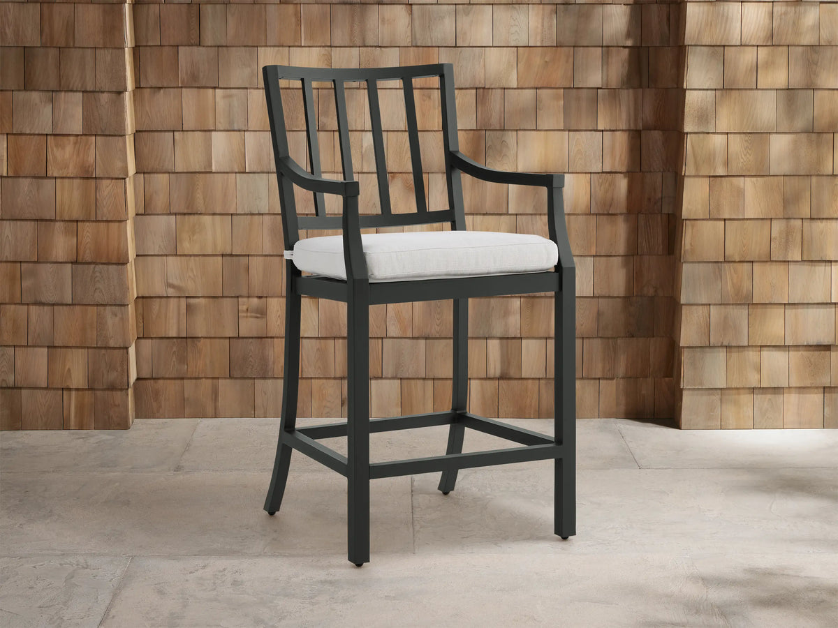 Montego Outdoor Aluminum Counter Stool, dark gray frame with slatted back and arms, white cushion. Angled on a patio.