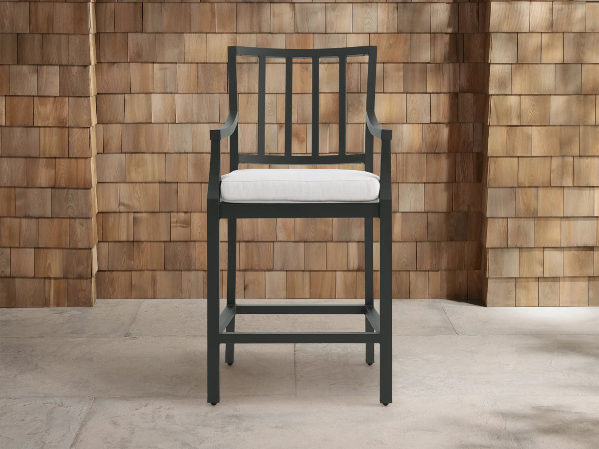 Montego Outdoor Aluminum Counter Stool, dark gray frame with slatted back and arms, white cushion. Angled on a patio.