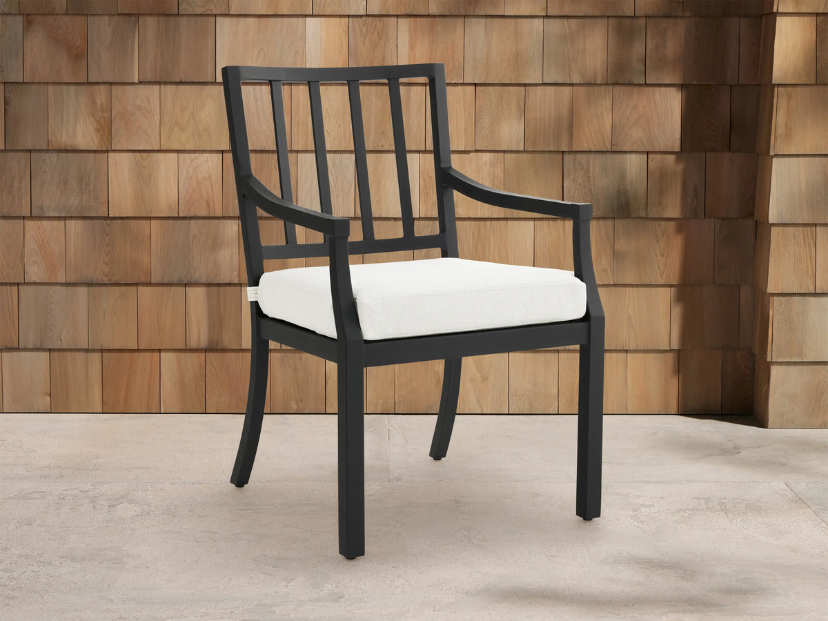 Montego Outdoor Aluminum Dining Arm Chair, black frame with slatted back, armrests & white cushion, shown angled on a patio.