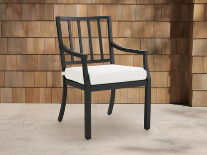Montego Outdoor Aluminum Dining Arm Chair, black frame with slatted back, armrests & white cushion, shown angled on a patio.