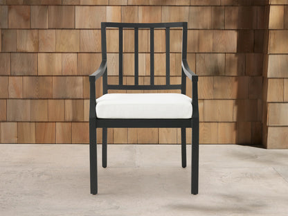 Montego Outdoor Aluminum Dining Arm Chair, black frame with slatted back, armrests & white cushion, shown angled on a patio.