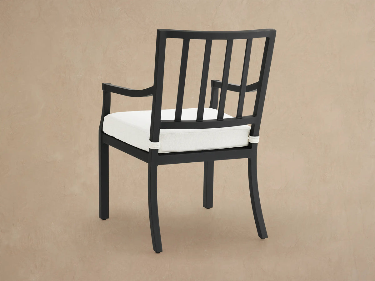 Angled close-up of Montego Outdoor Aluminum Dining Arm Chair. Matte black frame, slatted back, thick white cushion.