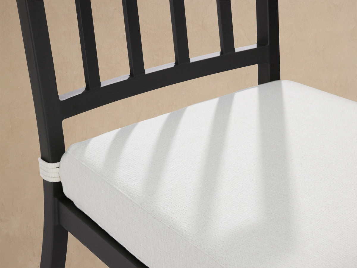 Dark gray aluminum Montego dining chair with light gray cushion, front view on patio against wood shingle wall.