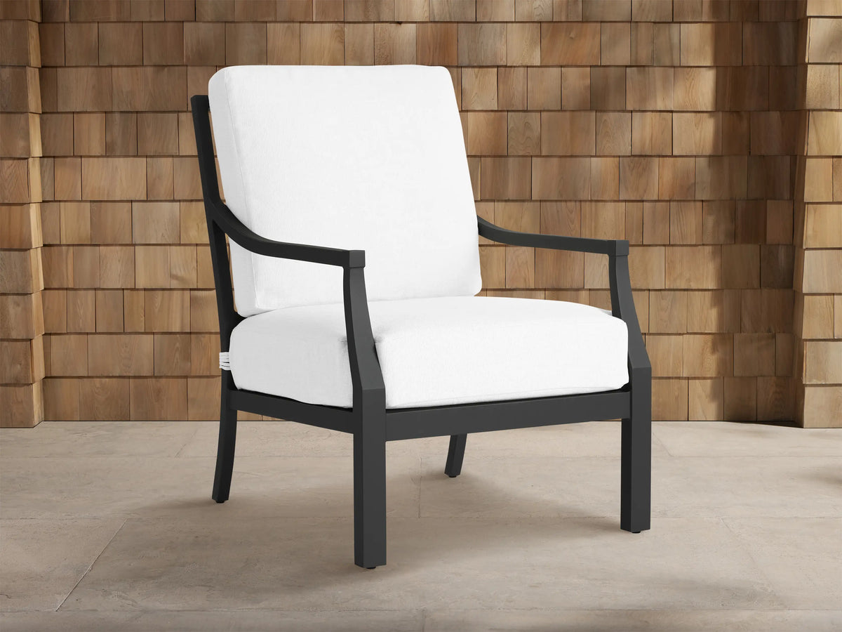 Montego Outdoor Aluminum Lounge Chair with a dark gray frame and thick white cushions, against a wooden shingle wall.