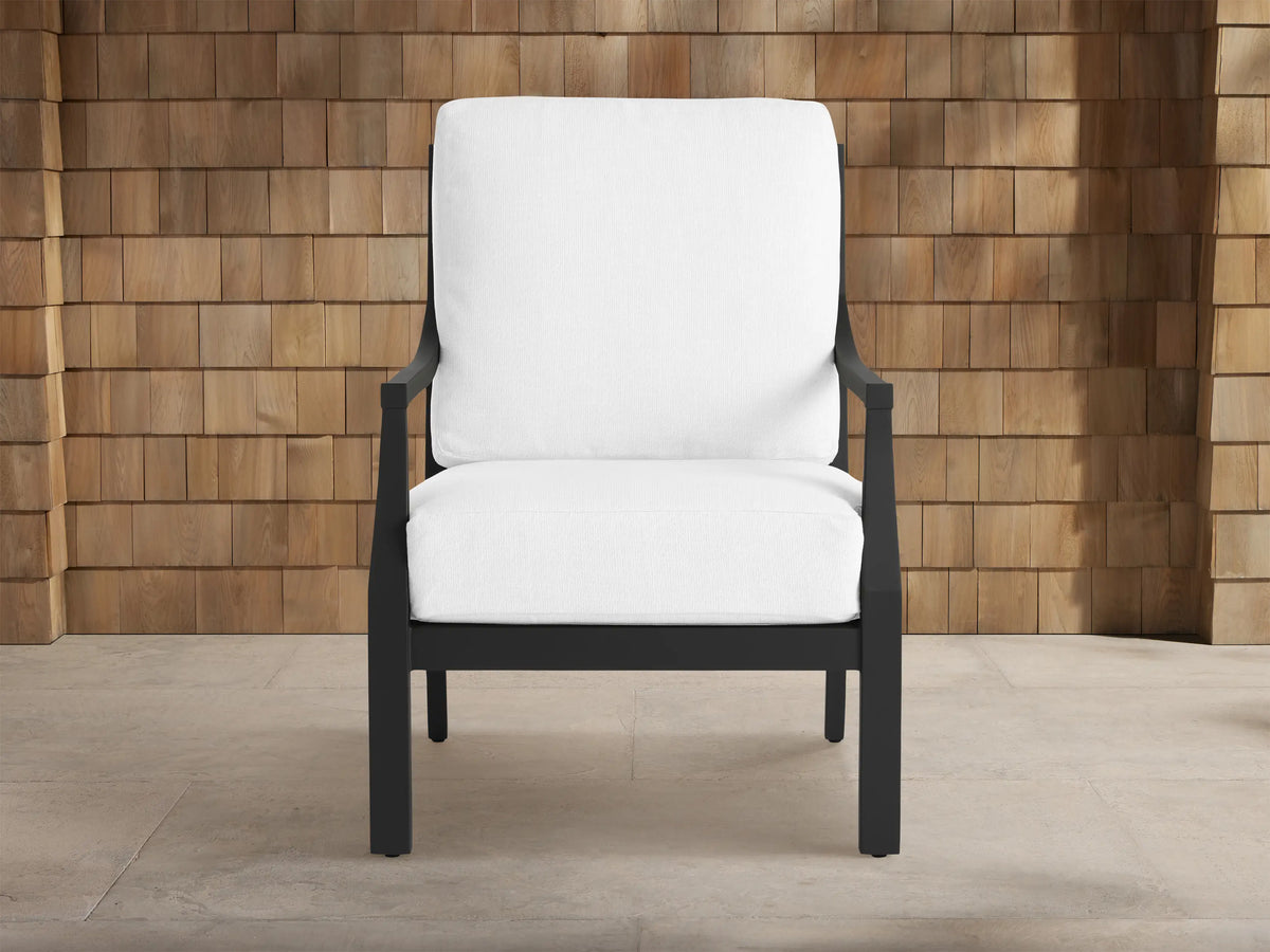 Montego Outdoor Aluminum Lounge Chair with a dark gray frame and thick white cushions, against a wooden shingle wall.