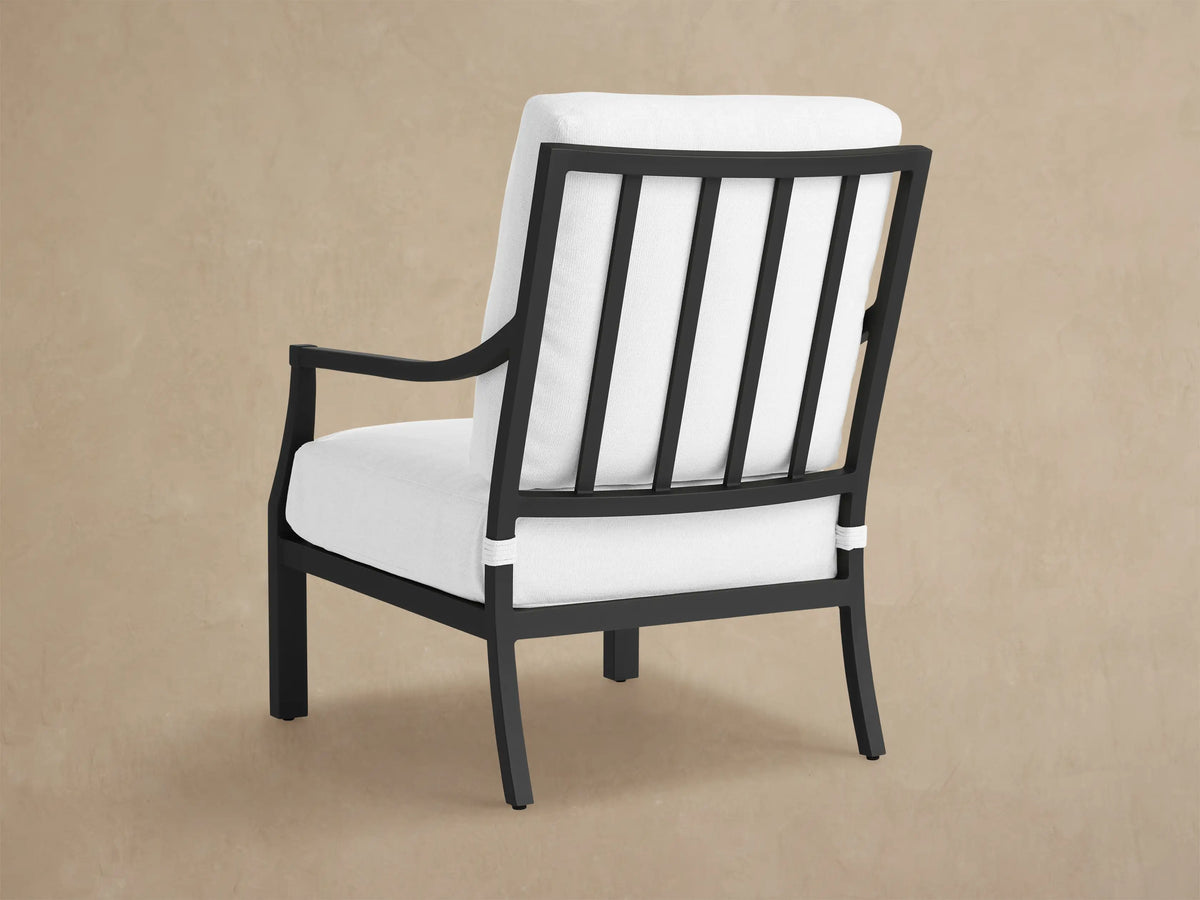 Close-up of Montego Outdoor Aluminum Lounge Chair with sleek black frame and thick white cushions against a light wall.