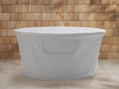 Three light grey Montego Outdoor Collection Covers on an outdoor sofa, chair, and bench, on a patio with a wooden wall.