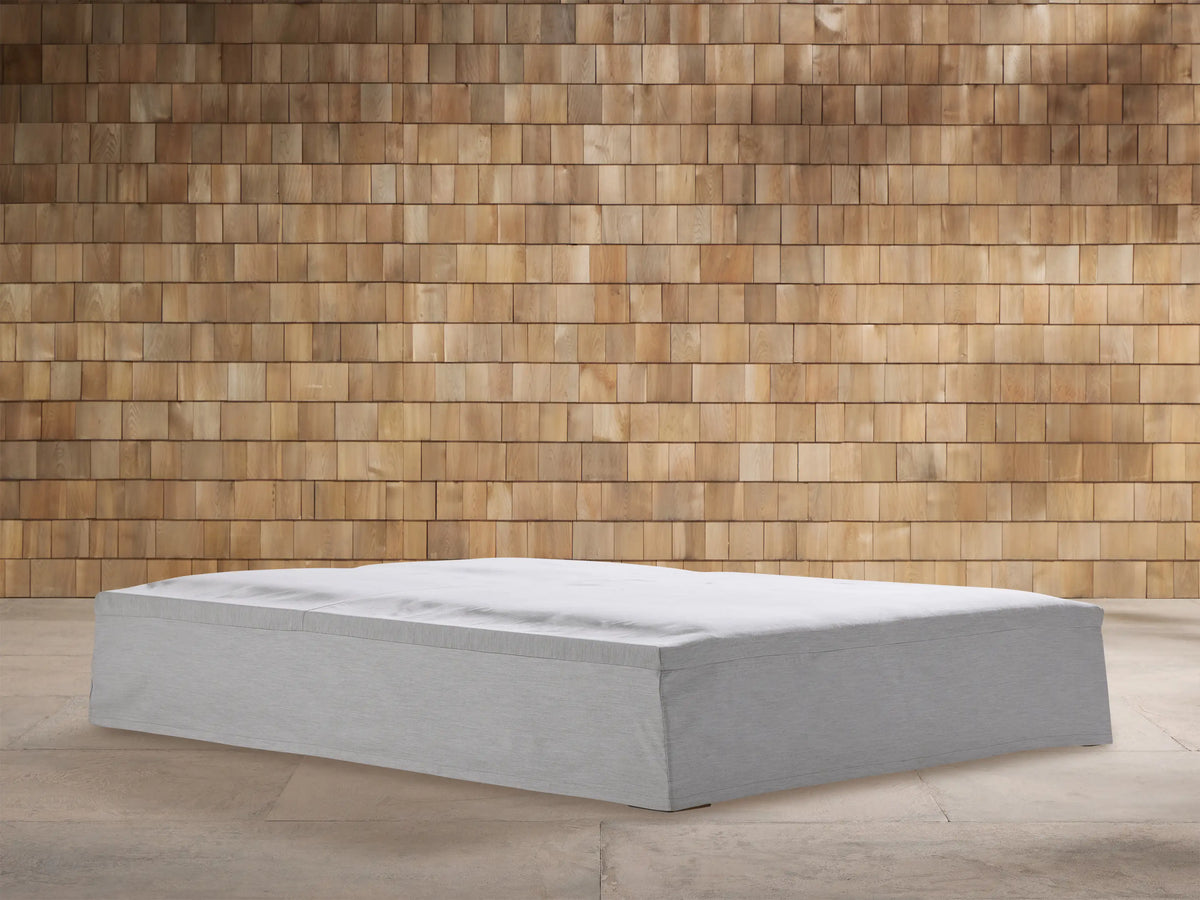 Light gray textured Montauk Outdoor Collection Cover on a rectangular outdoor furniture base, against a warm wooden shingle wall.