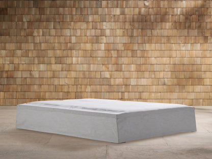 Light gray textured Montauk Outdoor Collection Cover on a rectangular outdoor furniture base, against a warm wooden shingle wall.