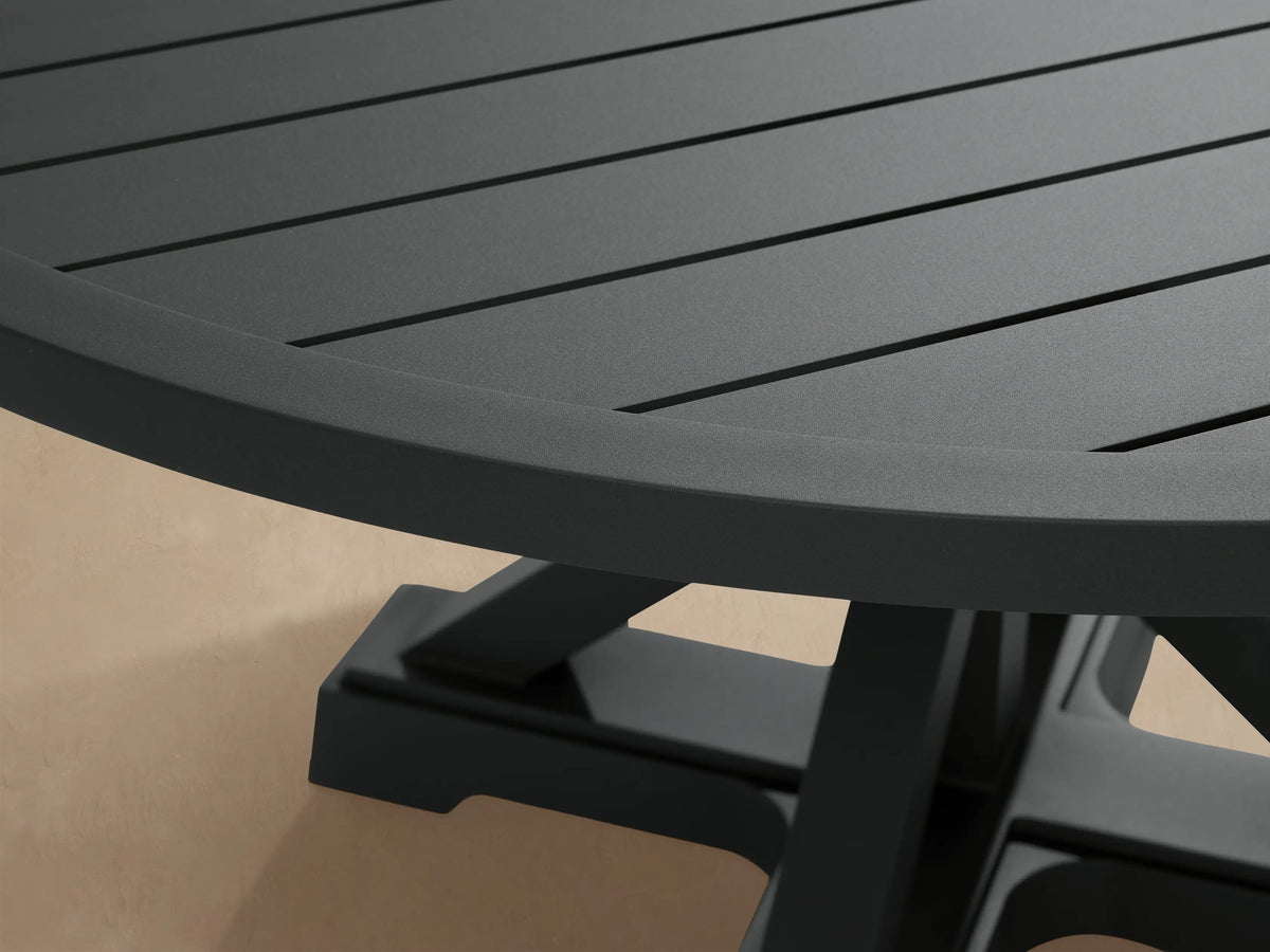 Montego Outdoor Aluminum Round Dining Table, charcoal gray, with a slatted top, X-pedestal base, on patio, wood shingle wall.