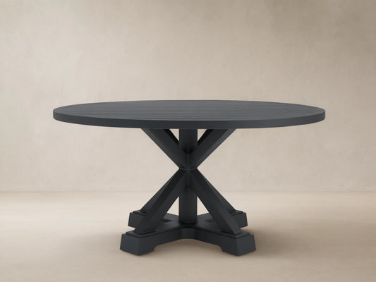 Montego Outdoor Aluminum Round Dining Table, charcoal gray, with a slatted top, X-pedestal base, on patio, wood shingle wall.