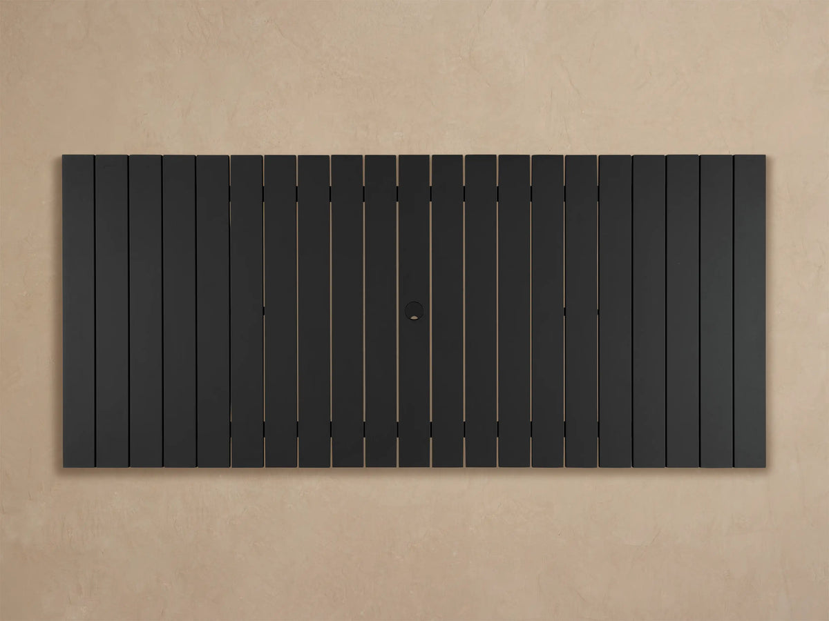 Close-up of Montego Outdoor Aluminum Dining Table. Dark gray slatted top and sturdy angled leg base on a light floor.
