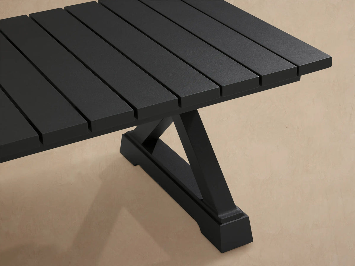 Montego Outdoor Aluminum Coffee Table, dark gray rectangular slat top, X-trestle base, on a patio with a wood shingle wall.