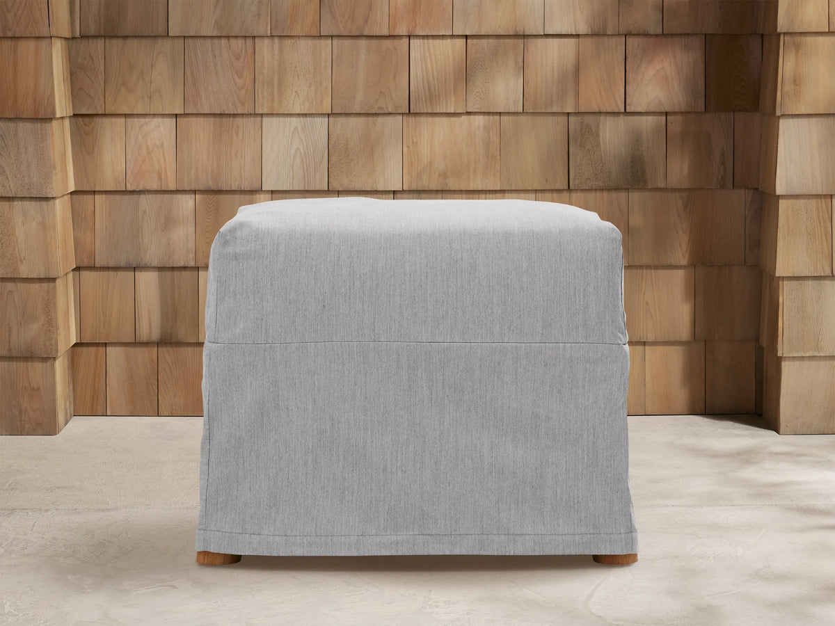 Three light gray Montego Outdoor Collection Covers: a sofa, armchair, and ottoman, on a patio with a wooden wall.